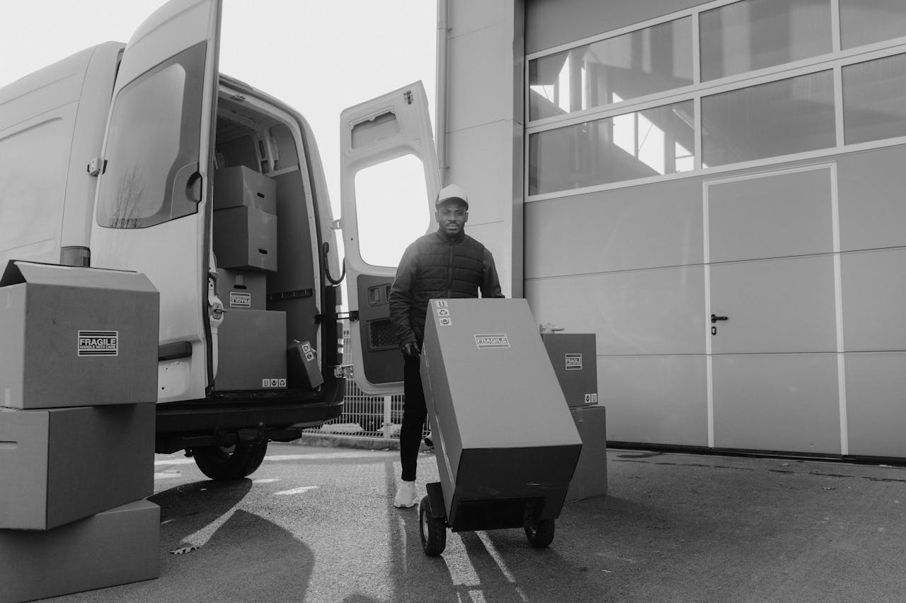 services-02 Monochrome image of a delivery man with boxes on a trolley near a van.