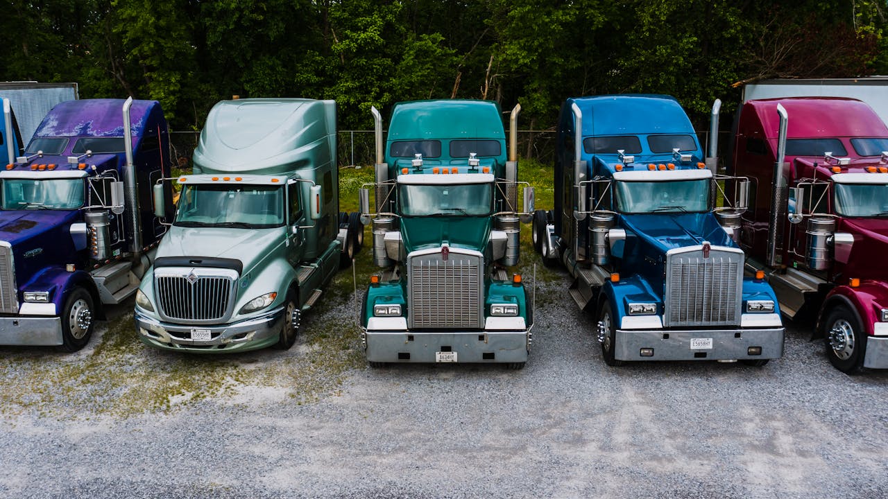 services-01 Row of vintage classic trucks of different colors parked on roadside outside warehouse against lush trees